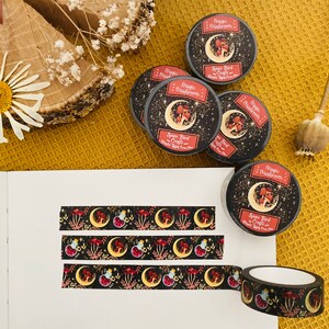 Op de afbeelding: Een set van vijf zwarte en gouden washi-tapes met een herhalend patroon van rode paddenstoelen, halve manen en sterren. De tapes zijn gelabeld met "Magic Mushrooms - Spooky Bird Crafts".