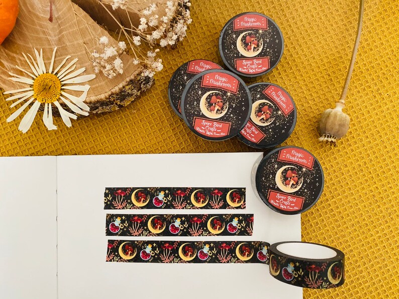 Op de afbeelding: Een set van vijf zwarte en gouden washi-tapes met een herhalend patroon van rode paddenstoelen, halve manen en sterren. De tapes zijn gelabeld met "Magic Mushrooms - Spooky Bird Crafts".