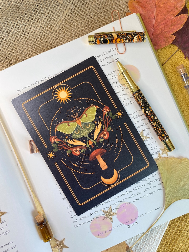 Peut inclure: Une carte noire avec une bordure dor&eacute;e repr&eacute;sente une lune, des &eacute;toiles, un champignon et un papillon de nuit vert aux ailes d&eacute;ploy&eacute;es. La carte porte l'inscription "The Bamboo-Cutter and the Moon-Child 63 III" en bas.