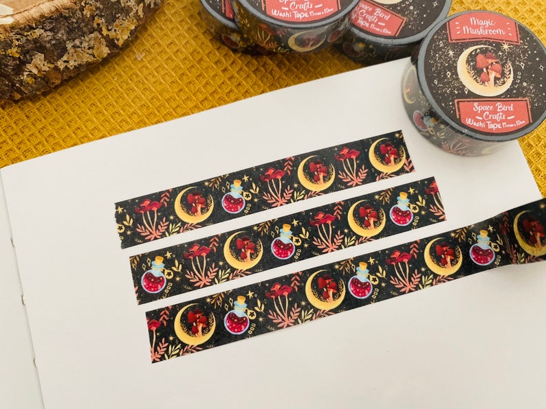 Op de afbeelding: Drie rollen washi tape met een donkere achtergrond en een herhalend patroon van manen, paddenstoelen en flesjes met toverdrank. De tekst op de tape luidt "Magic Mushroom" en "Sparrow Bird Crafts".