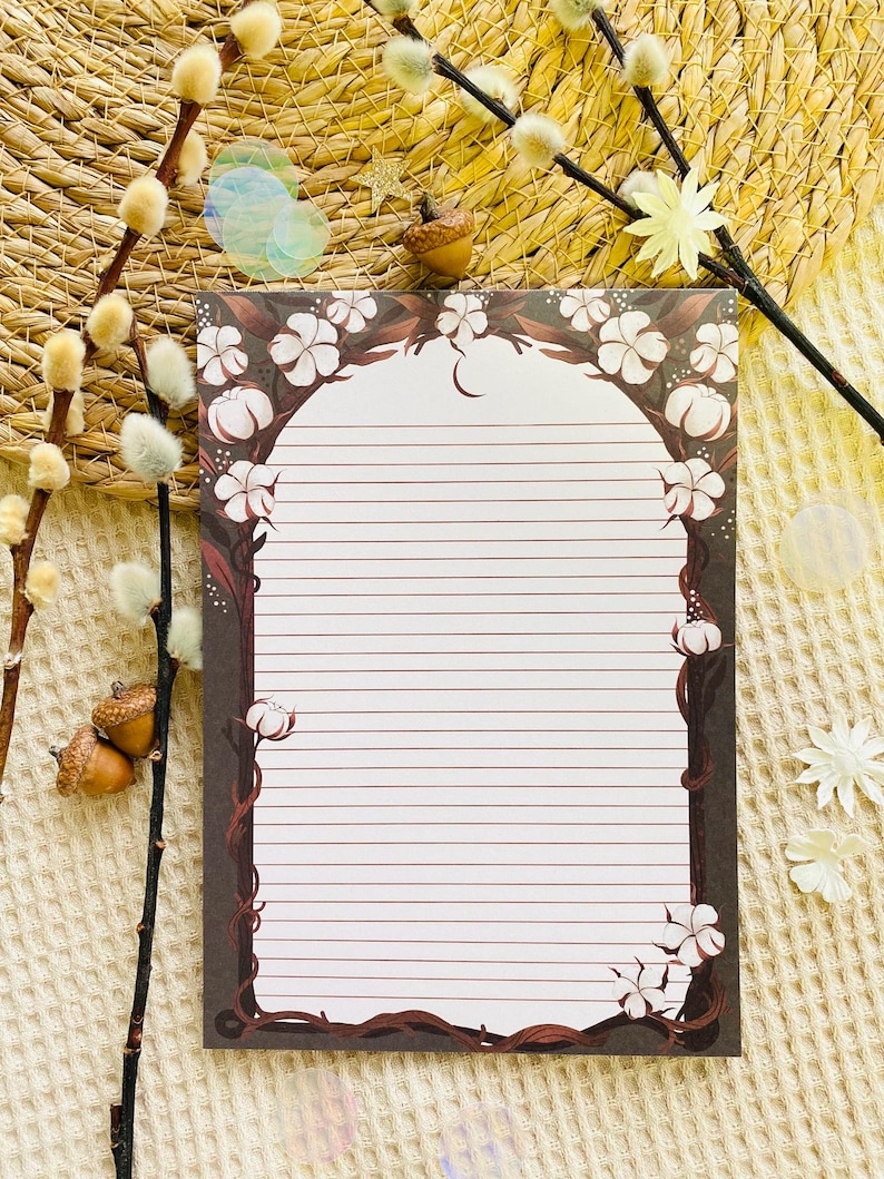 Pu&ograve; includere: Blocco note a righe con bordo floreale con fiori bianchi e tralci marroni. Il blocco note ha un bordo marrone scuro e un interno bianco con linee orizzontali. Elementi decorativi: ghiande e rametti.