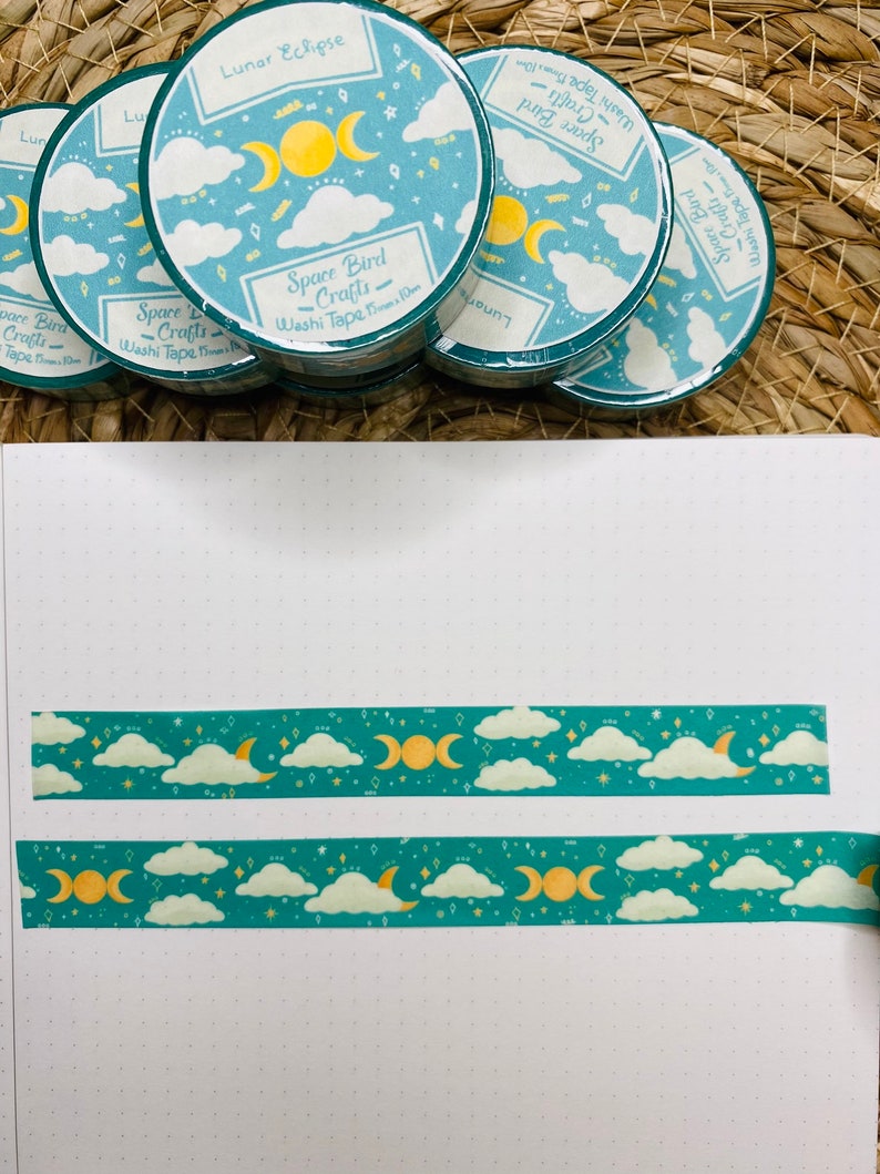 May include: A set of four teal and yellow washi tapes with a moon and stars design. The tapes are labeled "Space Bird Crafts" and "Lunar Eclipse".