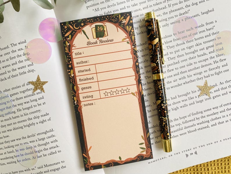 May include: A decorative book review card with a floral border and the words "Book Review" at the top. The card has spaces for title, author, and rating. A patterned pen rests beside the card.