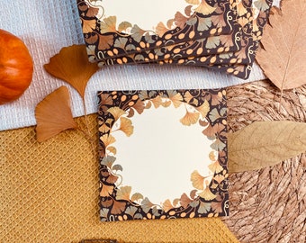 May include: A set of four brown and gold notepads with a ginkgo leaf design. The notepads are stacked on top of each other and have a white background with a gold border.