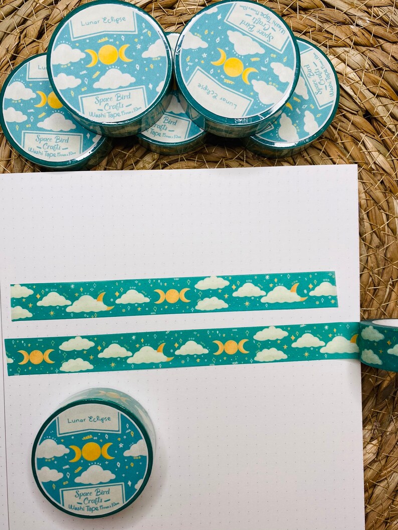 May include: A set of five teal blue washi tapes with a moon and cloud design. The tapes feature the text "Lunar Eclipse" and "Space Bird Crafts" with a gold crescent moon and stars.