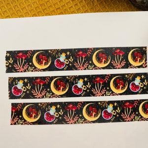 Op de afbeelding: Drie stroken washi tape met een herhalend patroon van manen, paddenstoelen en flesjes met toverdrank op een zwarte achtergrond. Het patroon is in tinten rood, goud en blauw.