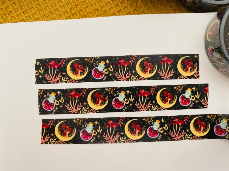 Op de afbeelding: Drie stroken washi tape met een herhalend patroon van manen, paddenstoelen en flesjes met toverdrank op een zwarte achtergrond. Het patroon is in tinten rood, goud en blauw.