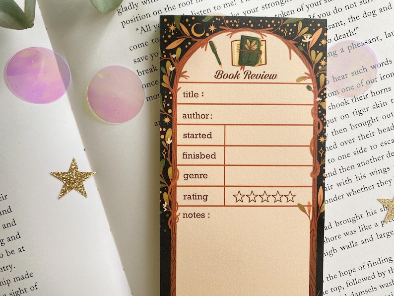 May include: A decorative bookmark with a book review template. The design features a book illustration, pen, and botanical elements. The bookmark includes fields for title, author, and rating.