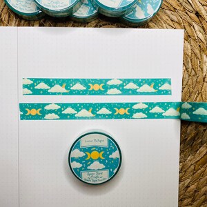 May include: A roll of teal washi tape with a moon and cloud pattern. The tape is unrolled and shows the design. The tape is labeled "Lunar Eclipse" and "Space Bird Crafts".