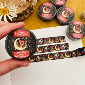 Op de afbeelding: Een rol zwarte en rode washi tape met een ontwerp van paddenstoelen, manen en sterren. De tape is gelabeld "Magic Mushroom - Space Bird Crafts - Washi Tape (10mm)"