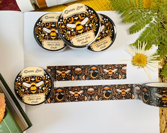 Pode incluir: Quatro rolos de fita washi com fundo preto e um padrão repetitivo de abelhas, flores e luas. A fita é etiquetada como "Queen Bee" e "Space Bird Crafts".