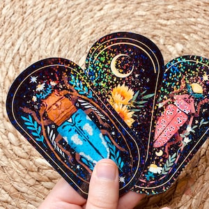 May include: Three iridescent holographic stickers featuring detailed illustrations of beetles with floral and celestial elements on a black background.