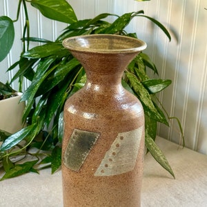 Könnte beinhalten: Eine braune Keramikvase mit einer breiten Öffnung und einer gesprenkelten Glasur. Die Vase hat ein geometrisches Design mit grünen und weißen Akzenten.