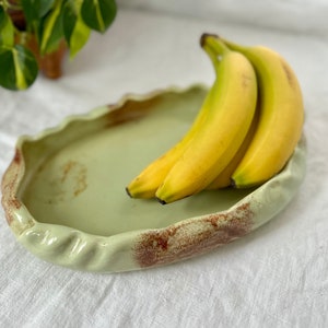 May include: A light green ceramic serving tray with a wavy edge and brown speckles. Three yellow bananas are arranged on the tray.