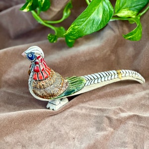 Könnte beinhalten: Eine Keramikfigur eines Fasanen mit einem weißen, braunen, roten, grünen und blauen Maldesign. Der Fasan hat einen langen Schwanz und steht auf einer braunen Oberfläche.