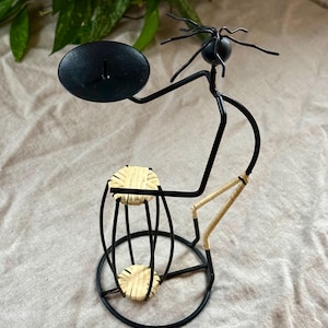 May include: Black metal candle holder shaped like a person holding a candle plate and a woven basket.