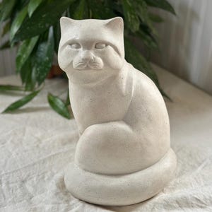 Op de afbeelding: Een wit keramiek kattenbeeld met een gespikkelde afwerking. De kat zit met zijn hoofd lichtjes gekanteld.