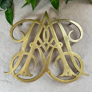 May include: A gold-toned metal trivet in the shape of the letter "A". The trivet has a decorative, intricate design.