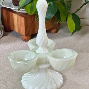 Peut inclure: Porte-œufs en verre laiteux blanc avec une poignée torsadée et trois coupelles individuelles pour les œufs. Le porte-œufs a une base festonnée.