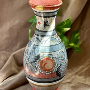 Può includere: Un vaso in ceramica dipinto a mano con un corpo largo e rotondo e un collo stretto. Il vaso è decorato con un motivo floreale in tonalità di blu, rosso e oro. Il vaso ha un aspetto rustico e vintage.
