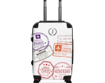 May include: White suitcase with a black handle and wheels. The suitcase is decorated with colorful travel stamps from various countries, including Paris, Amsterdam, Tokyo, and Hong Kong. The stamps include arrival dates and airport codes.
