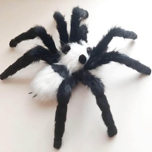 May include: A plush toy spider with a panda bear design. The spider has a white and black body, with eight black legs. The spider's head is white with black eyes and a black nose. The toy is made of soft, furry material.