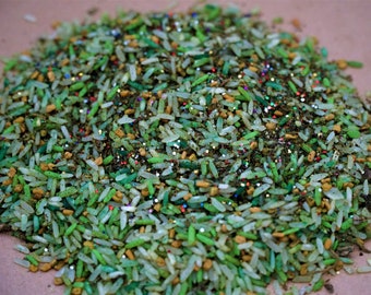 May include: A close-up of a pile of decorative rice, with a mix of green, yellow, and white grains. The rice is sprinkled with colorful glitter, creating a festive and textured appearance. The grains are of varying sizes and shapes.