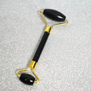 May include: A black jade roller with a gold handle. The roller is used for facial massage.