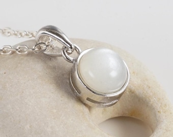 May include: A silver necklace with a white moonstone pendant. The pendant is set in a silver bezel and has a smooth, round shape.