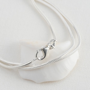 Op de afbeelding: Een zilveren slangenketting met een karabijn sluiting.