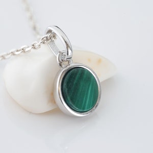 Peut inclure: Un collier en chaîne argent avec un pendentif rond orné d'une pierre de malachite verte.