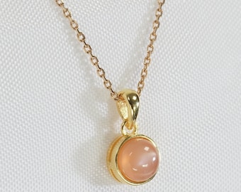 May include: A gold chain necklace with a round pendant featuring a light pink gemstone.