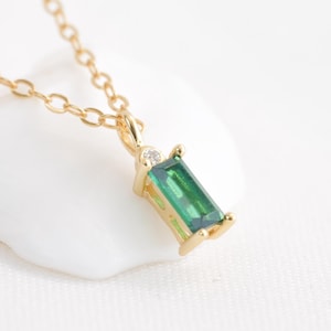 Puede incluir: Un collar de cadena de oro con un colgante de piedra preciosa verde. El colgante tiene forma rectangular con un pequeño acento de diamante.