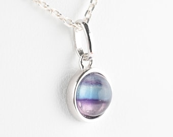 Puede incluir: Un collar de cadena de plata con un colgante redondo con una piedra preciosa de fluorita azul, púrpura y verde.