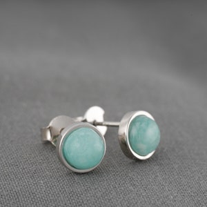 May include: A pair of silver stud earrings with round, light blue gemstones.