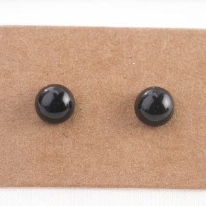 Op de afbeelding: Een paar zwarte oorbel studs op een bruine kaart.