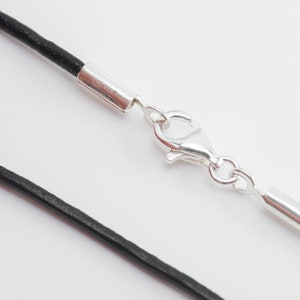 Peut inclure: Un collier en cordon de cuir noir avec des embouts argentés et un fermoir mousqueton argenté.