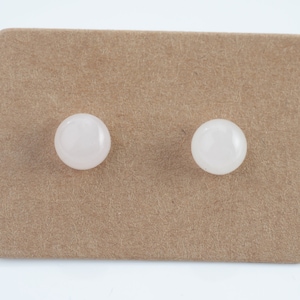 Op de afbeelding: Een paar witte edelsteen oorbel studs gepresenteerd op een bruine kaart.