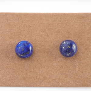 May include: A pair of blue lapis lazuli stud earrings with gold flecks on a brown background.
