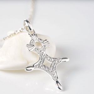 May include: A silver pendant necklace with a detailed, intricate design. The pendant is shaped like a cross with a circle in the center. The necklace is on a white background.