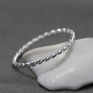Peut inclure: Une bague en argent torsadée, posée sur un coquillage blanc.