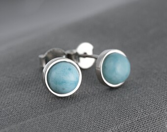 May include: A pair of silver stud earrings with round, light blue gemstones.