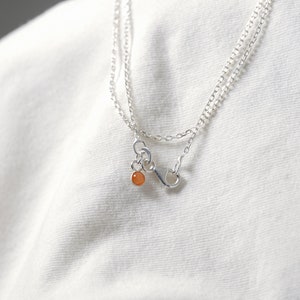 May include: A silver chain necklace with a small orange gemstone pendant.