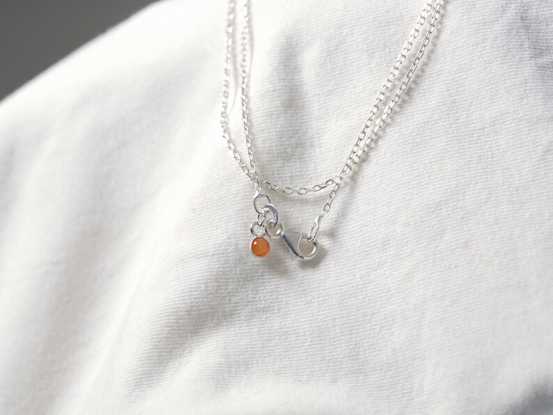 May include: A silver chain necklace with a small orange gemstone pendant.