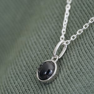 Puede incluir: Un collar de cadena de plata con un colgante de piedra negra.