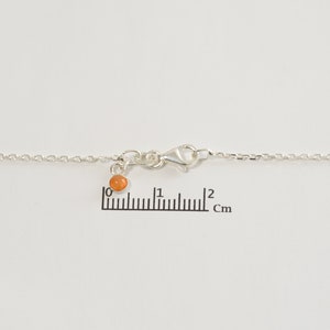 May include: A silver chain necklace with a small orange bead charm. The chain is 2 cm long.