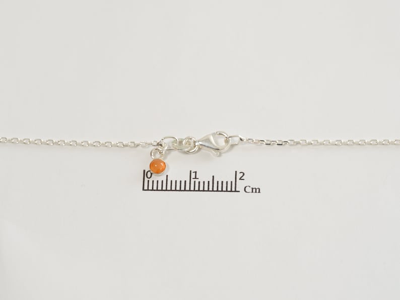 May include: A silver chain necklace with a small orange bead charm. The chain is 2 cm long.