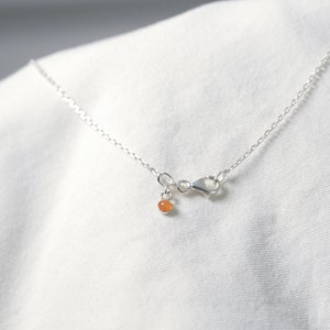 May include: A silver chain necklace with a small orange gemstone pendant.