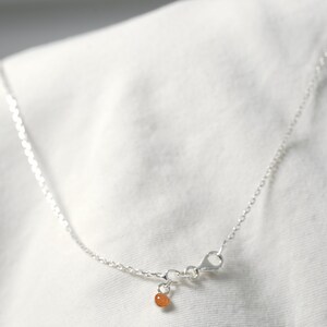 May include: A silver chain necklace with a small orange bead charm. The chain is delicate and has a lobster clasp.
