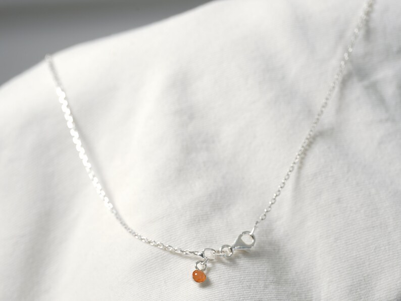 May include: A silver chain necklace with a small orange bead charm. The chain is delicate and has a lobster clasp.